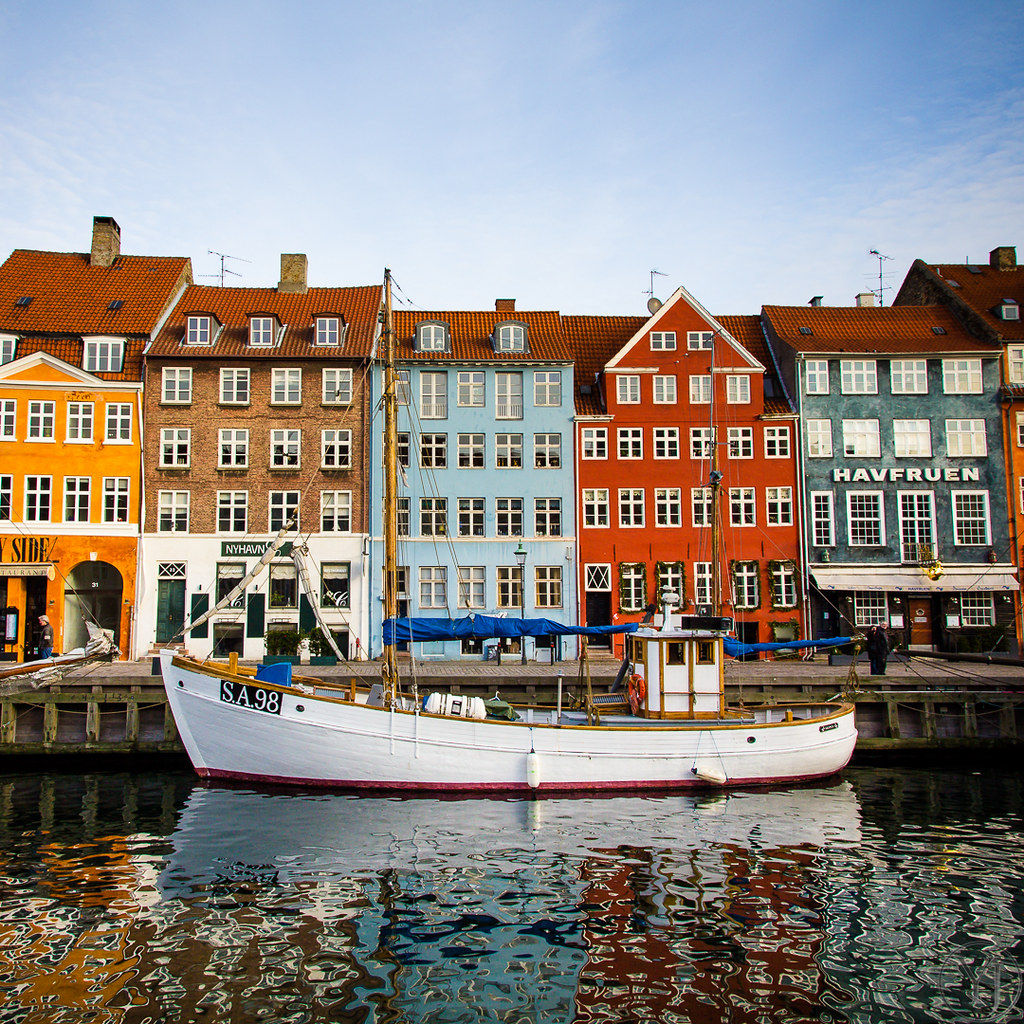 Historic colorful waterfront buildings in Copenhagen with a white wooden boat docked on a calm canal reflecting the vibrant facades.