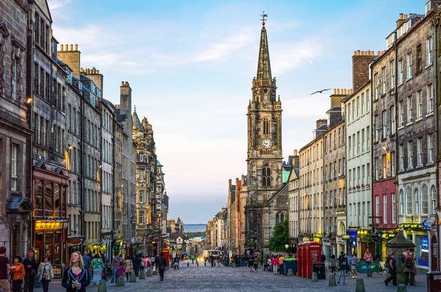 Historic view of Edinburgh’s Royal Mile with stone buildings, shops, and pedestrians on a sunny day in Scotland
