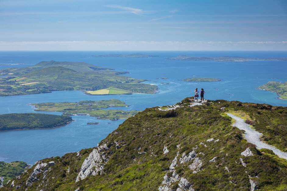 Hikers walking along the scenic Diamond Hill trail in Connemara National Park with sweeping mountain and valley views under a bright sky