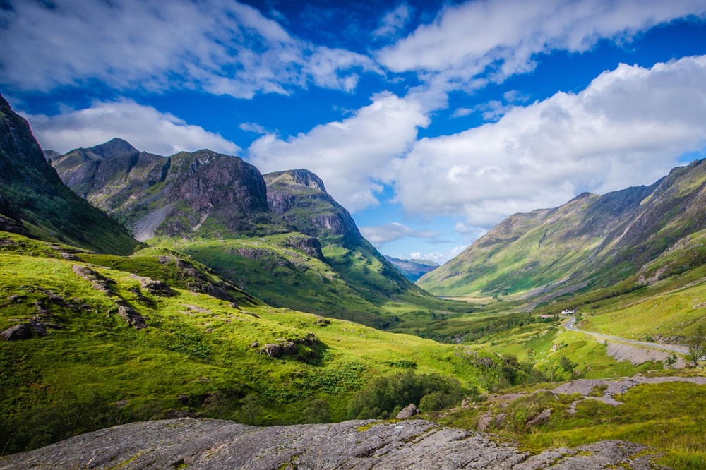 Scenic view of Glencoe with dramatic mountains, a winding valley, and soft light highlighting the rugged Highland landscape.