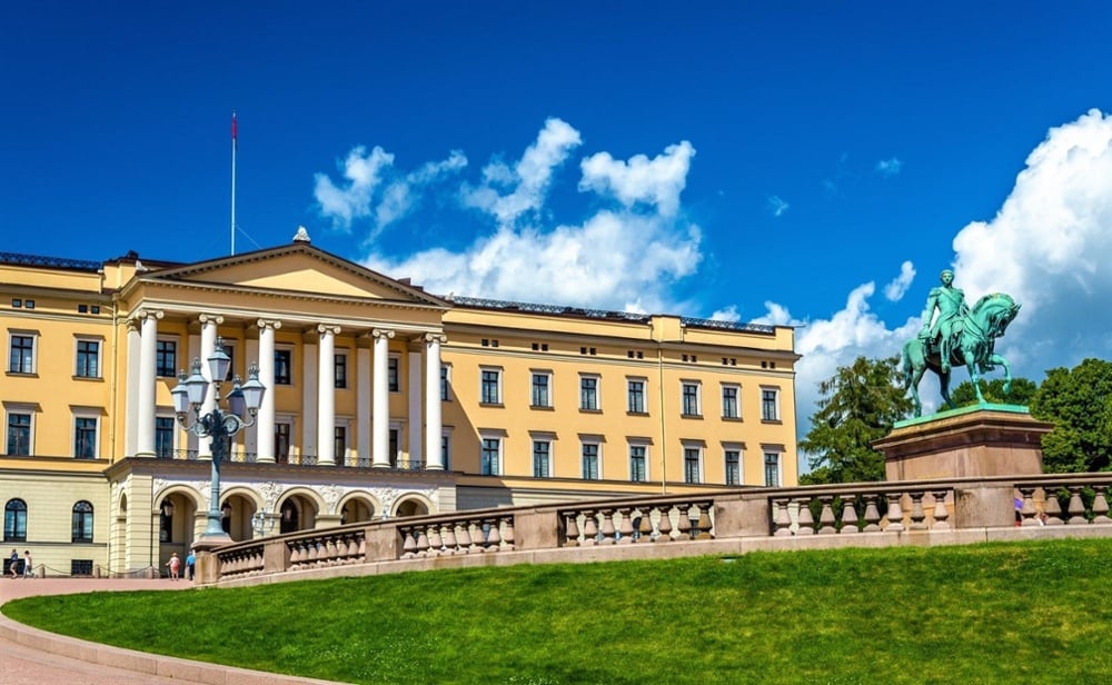 Oslo Royal Palace with yellow neoclassical facade, equestrian statue, and green lawn under a blue sky with clouds