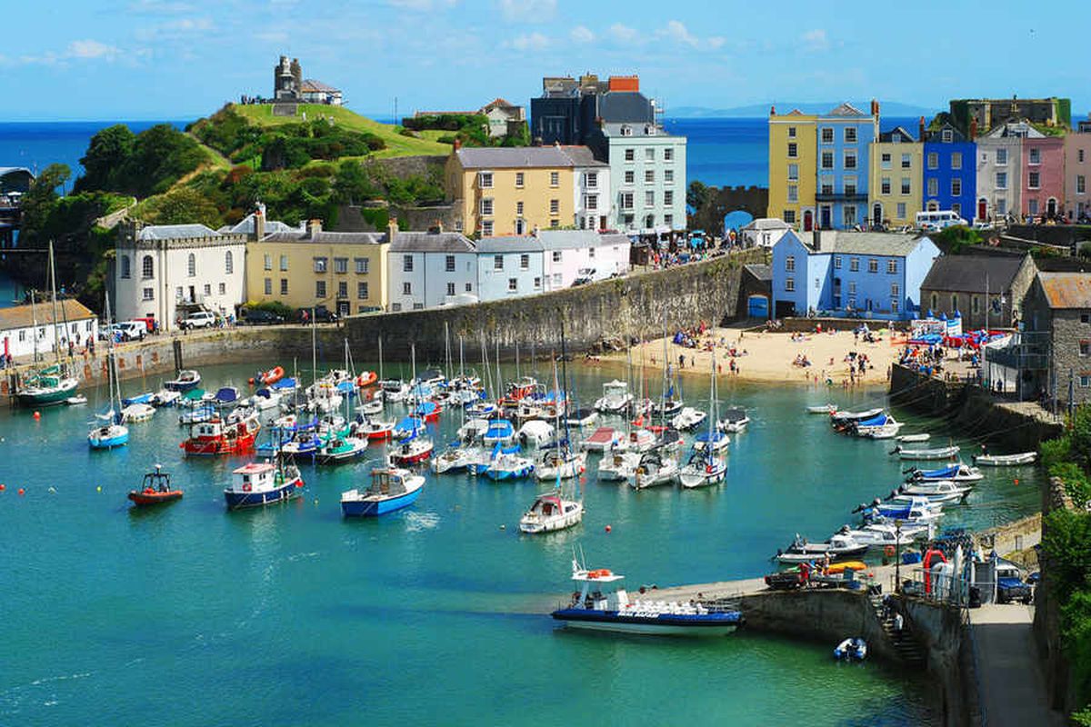 Tenby Harbour in Wales with colorful seaside buildings, boats, and calm water under a bright sky